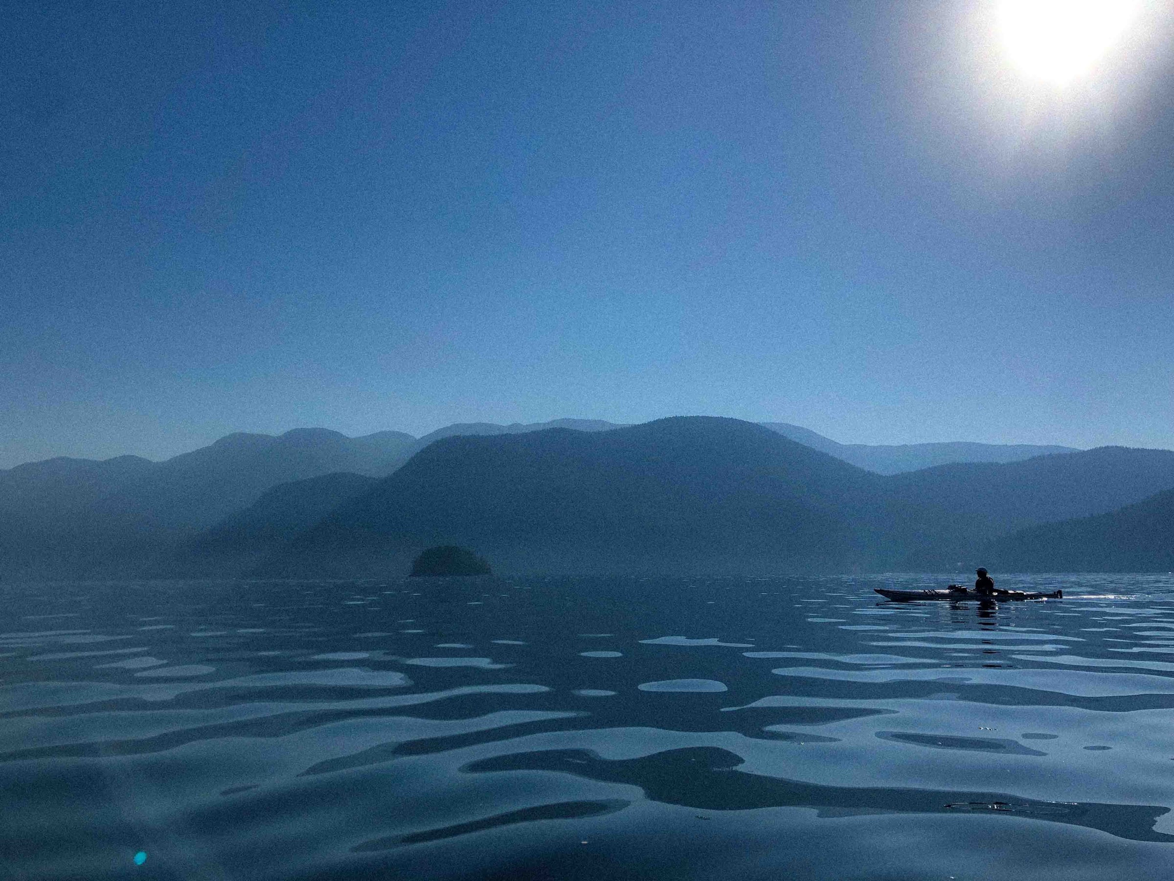 A kayaker crossing calm water beneath the mountains